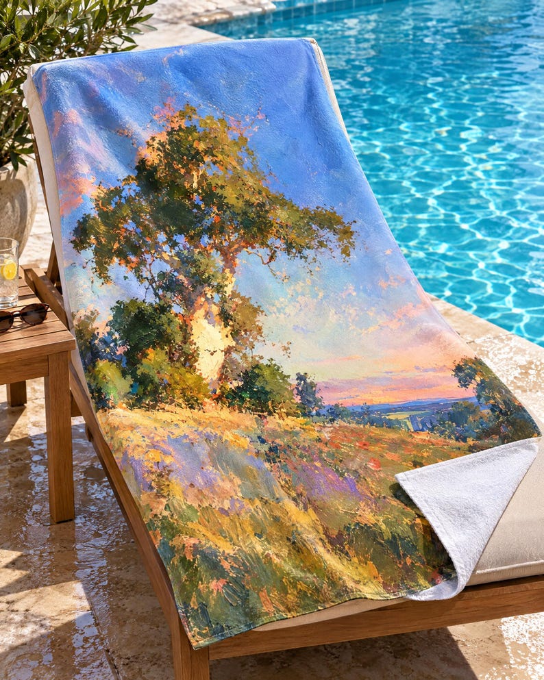 May include: A rectangular beach towel featuring an impressionistic landscape painting of a large tree on a grassy hill under a blue sky. The artwork displays vibrant shades of green, yellow, orange, and blue, with a white underside visible at the corner.
