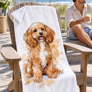 Cavapoo beach towel draped over a wooden Adirondack chair on a seaside deck, a top corner folded back to the white terry back; a man in sunglasses and a linen shirt sits nearby holding a drink.