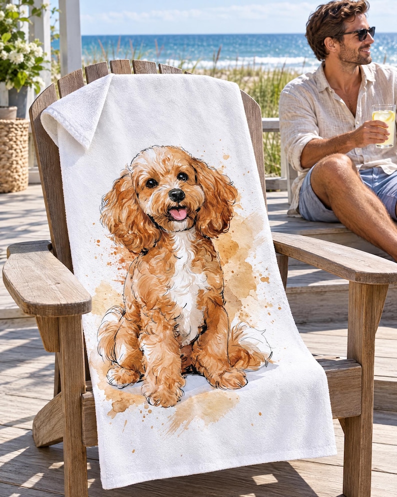 Cavapoo beach towel draped over a wooden Adirondack chair on a seaside deck, a top corner folded back to the white terry back; a man in sunglasses and a linen shirt sits nearby holding a drink.
