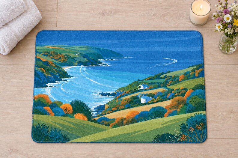 Overhead view of the whole cliffside cottage bath mat on a light wood floor, with rolled white towels, a lit candle and a small glass vase of wildflowers beside it.