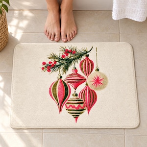 Retro Christmas ornament bath mat on a tiled floor in front of a white bathtub: six striped pink, olive and cream baubles hang from a pine sprig with red berries on a cream background; bare feet stand at the edge nearest the tub.