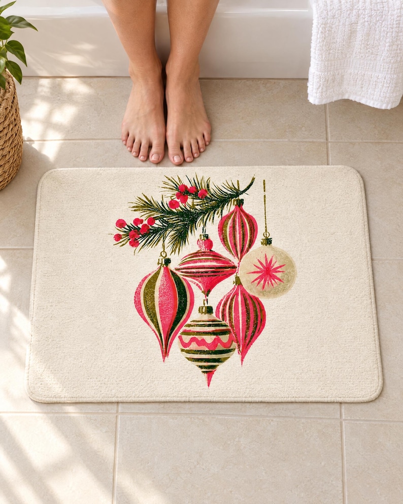 Retro Christmas ornament bath mat on a tiled floor in front of a white bathtub: six striped pink, olive and cream baubles hang from a pine sprig with red berries on a cream background; bare feet stand at the edge nearest the tub.