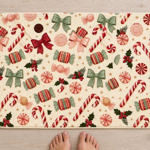 Candy cane Christmas bath mat seen from above on a light wood floor, with rolled white towels, a candle, pine sprigs and bare feet at the bottom edge.