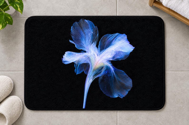 May include: A rectangular bath mat with a solid black background featuring a large, central, ethereal blue flower graphic. The petals display translucent, wispy textures in shades of deep navy, bright cobalt, and soft violet, radiating from a pale centre.