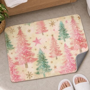 Pink Christmas tree bath mat in front of a wood vanity, one corner turned up to show the gray anti-slip back, with white slippers below.