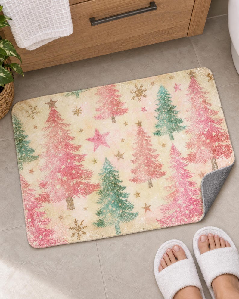 Pink Christmas tree bath mat in front of a wood vanity, one corner turned up to show the gray anti-slip back, with white slippers below.