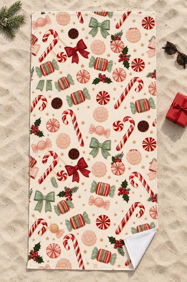 Candy cane Christmas beach towel laid flat on sand with sunglasses and a small red gift box, one corner folded to show the white back.
