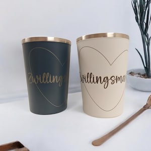 Könnte beinhalten: Zwei Keramikbecher mit goldenen Rändern und einem goldenen Herzdesign. Die Becher haben den Text "Twinlings" und "Twinlingsma" aufgedruckt.