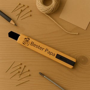 Könnte beinhalten: Ein hellbrauner Brieföffner im Bambus-Stil mit den Worten "Bester Papa" und einem Bild von Vater und Kind. Der Öffner hat eine schwarze Klinge und ist von goldenen Pins, einem Bleistift und Bindfaden umgeben.