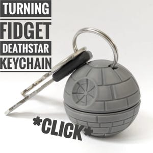 Peut inclure: Un porte-clés fidget Death Star gris avec un porte-clés et des clés argentés. Le porte-clés a une surface détaillée et le texte "TURNING FIDGET DEATHSTAR KEYCHAIN" et "*CLICK*".