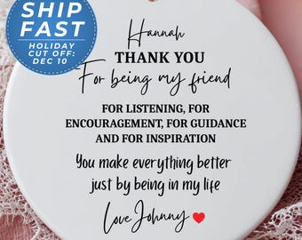 May include: A white ceramic ornament with a black string for hanging. The ornament has the text "Hannah THANK YOU For being my friend" and other sentiments. A blue and white tag says "SHIP FAST" and "HOLIDAY CUT OFF: DEC 10".