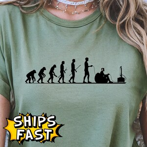 May include: Olive green t-shirt featuring a black silhouette of human evolution, culminating in a person gaming. The shirt includes the text "SHIPS FAST" in a yellow burst.