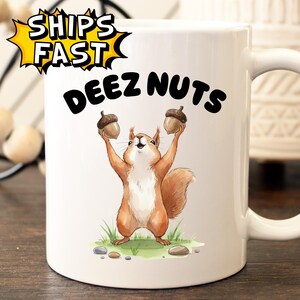May include: White ceramic mug featuring a cartoon squirrel holding two acorns, with the text "DEEZ NUTS" above the squirrel. The mug also has the text "SHIPS FAST" in a yellow burst.