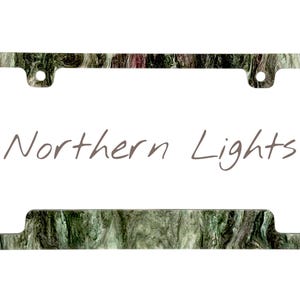 May include: License plate frame with a marbled green, brown, and white pattern. The frame has the words "Northern Lights" in a handwritten style font. The frame has two holes at the top for mounting.