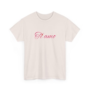 May include: Cream-colored t-shirt with the Italian phrase "Ti amo" in a cursive, reddish-pink font. The text is centered on the front of the shirt. The shirt has short sleeves and a crew neck.