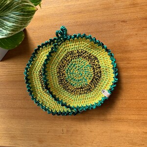 Peut inclure: Deux maniques en crochet de couleur jaune, verte et noire avec un bord festonné. Les maniques sont de forme circulaire et ont une boucle pour les suspendre.