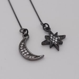 May include: A pair of black dangle earrings with a crescent moon and a star charm. Both charms are adorned with clear rhinestones.