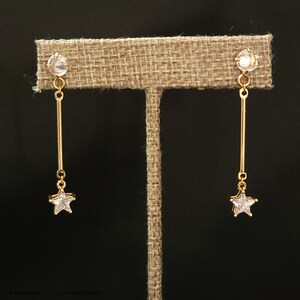 May include: A pair of gold earrings with a star-shaped pendant and clear crystal stones.