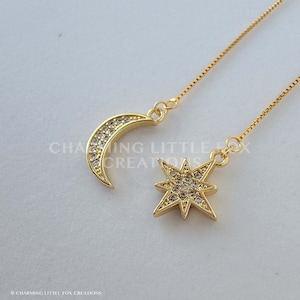 Puede incluir: Un par de pendientes de oro con un creciente de luna y un encanto de estrella. Ambos encantos están adornados con brillantes diamantes de imitación transparentes.
