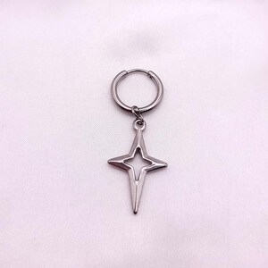May include: A single silver-colored earring with a star-shaped pendant. The earring features a hoop design with a star pendant hanging from it. The star has a four-pointed design with a cutout in the center. The earring is displayed against a white background.
