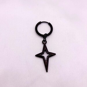 May include: A single black earring featuring a hoop and a dangling four-pointed star pendant. The star has a hollow center and a pointed design. The earring is set against a white background.
