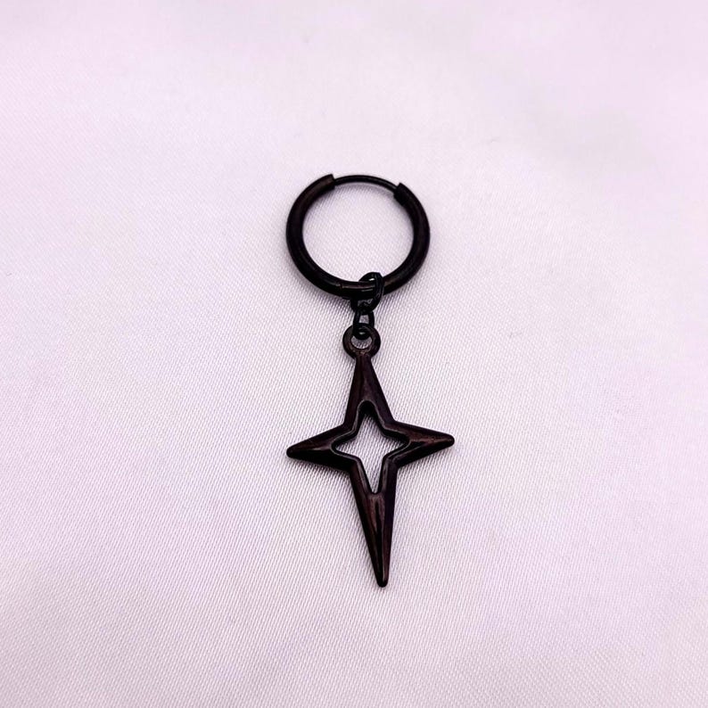 May include: A single black earring featuring a hoop and a dangling four-pointed star pendant. The star has a hollow center and a pointed design. The earring is set against a white background.