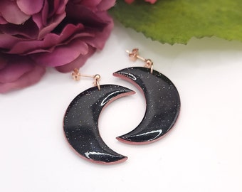 May include: A pair of black crescent moon earrings with rose gold accents and glitter embedded in the black enamel.