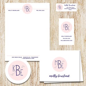 May include: A set of stationery featuring a pink circle with a navy blue monogram. The monogram is "KBE" with a decorative flourish. The stationery includes a letterhead, business card, and note card. The letterhead has the name "Kelly Bourland" and contact information. The business card has the name "Kelly Bourland" and contact information. The note card has the name "molly bourland" and the monogram "MBE".