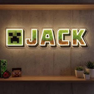Pode incluir: Uma placa de néon com a palavra "JACK" em uma fonte inspirada no Minecraft. As letras são preenchidas com texturas de grama e terra, delineadas em branco e colocadas contra uma parede de concreto cinza. Um quadrado pixelado verde está à esquerda. A placa está montada acima de uma prateleira de madeira.