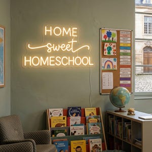 May include: A wall-mounted neon sign emitting a warm yellow glow, displaying the text "HOME sweet HOMESCHOOL" in a combination of block and cursive lettering. The sign features a clear acrylic backing and is powered by a thin white cord.