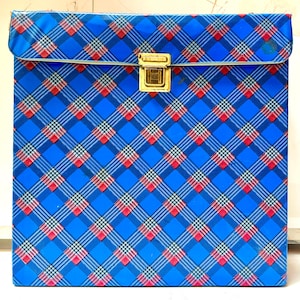 May include: A square storage case featuring a vibrant blue, red, and white plaid pattern. The case has a hinged lid that secures with a gold-toned metal latch centered on the front. The exterior surface has a smooth, glossy finish throughout.