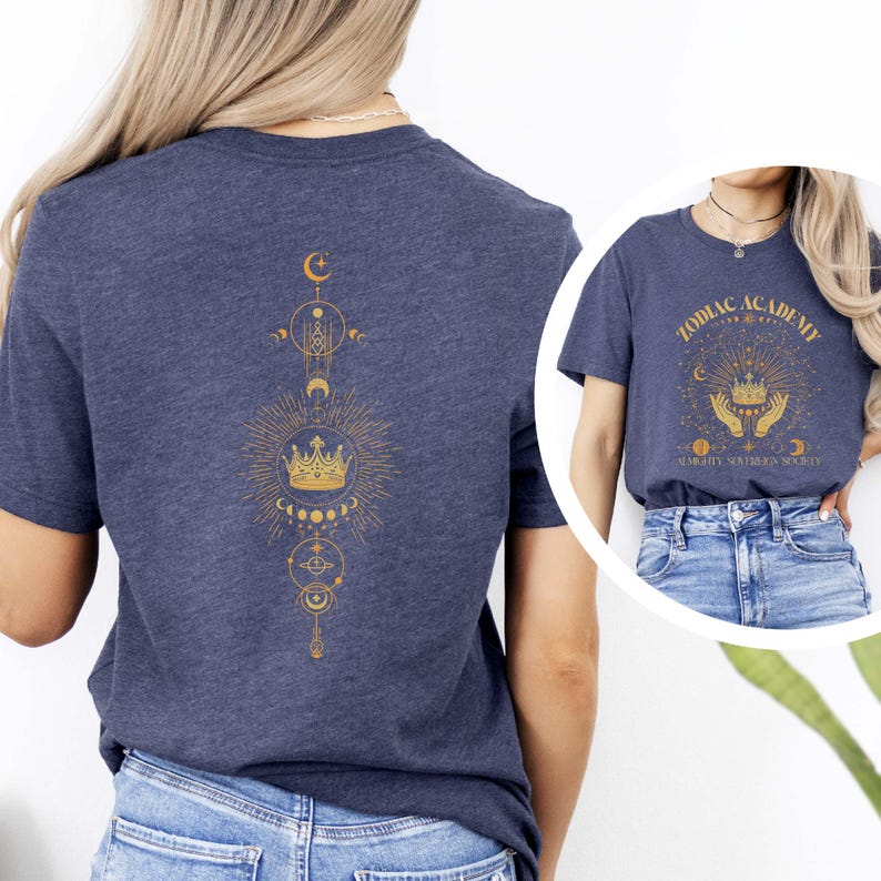 Pu&ograve; includere: Due t-shirt blu navy con disegni dorati a tema zodiacale. La parte anteriore di una t-shirt presenta il testo "Zodiac Academy" con una corona e mani che tengono la corona. La parte posteriore dell'altra t-shirt presenta una corona con un design di luna e stelle.