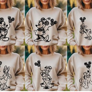 May include: Six beige sweatshirts with different black and white cartoon character designs. The designs include Mickey Mouse, Minnie Mouse, Donald Duck, Goofy, and Pluto.