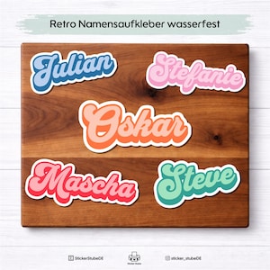 Könnte beinhalten: Eine Auswahl an Namensaufklebern im Retro-Stil in verschiedenen Farben, darunter Blau, Rosa, Orange und Grün, auf einer Holzoberfläche angeordnet. Die Aufkleber tragen Namen wie Julian, Stefanie, Oskar, Mascha und Steve. Der Text "Retro Namensaufkleber wasserfest" ist oben.
