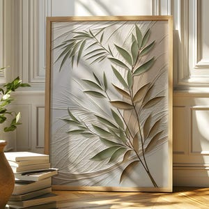 May include: A framed botanical art print with a relief of green leaves and branches on a white background. The artwork is displayed in a room with a wooden floor, a terracotta pot with a green plant, and a stack of books.
