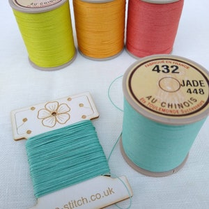 May include: A collection of colorful thread spools and a wooden thread holder. The spools are in shades of yellow, orange, and coral, with labels that read "432". A wooden thread holder with teal thread is also present, with the text "eco-stitch.co.uk".