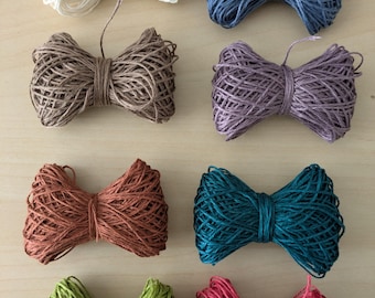May include: An assortment of eight decorative twine bows in various colors, including cream, blue, brown, purple, rust, teal, green, and pink. Each bow is meticulously crafted from tightly wound twine, showcasing a rustic and handcrafted aesthetic. Ideal for crafting and gift wrapping.