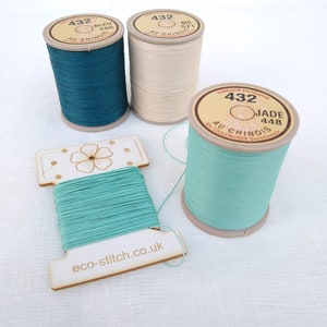 May include: An assortment of colorful thread spools and a wooden thread holder. The spools are teal, cream, and jade green, with labels that read "432" and other text. The wooden holder has a floral design and the text "eco-stitch.co.uk".