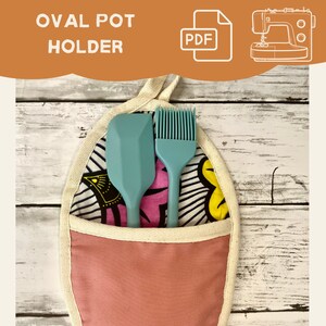 May include: A pink oval pot holder with a white trim and a black and white patterned fabric lining. Two kitchen utensils, a blue spatula and a blue silicone brush, are tucked inside the holder.