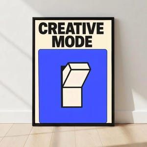 May include: A framed art print with the words "CREATIVE MODE" in bold black letters at the top. Below, a blue square features a white, stylized on/off switch graphic. The background is a light beige color.