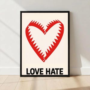 May include: Framed art print featuring a red heart-shaped design with jagged edges, resembling a bear trap, on a cream background. The words "LOVE HATE" are printed in black below the heart. The artwork is in a black frame.