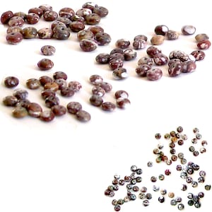 May include: A collection of brown, white, and gray speckled round beads with two holes in each bead. The beads are scattered on a white surface.