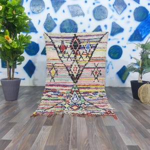 May include: A colorful Moroccan rug with a diamond pattern in shades of pink, blue, green, and yellow. The rug has a white background and is woven with a variety of textures.