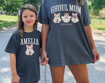 May include: A matching set of two grey t-shirts with a ghost graphic. The adult shirt says "Ghoul Mom Est. 2014" and the child's shirt says "Amelia".