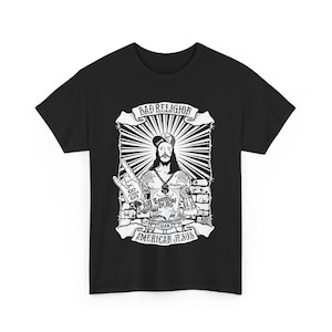 May include: Black t-shirt with a white graphic of a tattooed Jesus figure wearing a baseball cap and holding a peace sign. The graphic includes the text "Bad Religion", "Go Jesus Go", "Too High To Die", "USA", and "American Jesus".