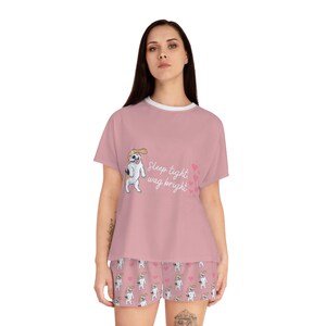 Könnte beinhalten: Rosafarbener Pyjama-Set mit einem kurzärmeligen Oberteil und einer Hose. Das Oberteil zeigt einen Cartoon-Hund mit dem Text "Sleep tight, wag bright". Die Hose hat ein sich wiederholendes Muster des Cartoon-Hundes.