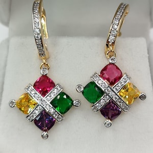 Peut inclure: Une paire de boucles d'oreilles dorées avec un motif géométrique. Chaque boucle d'oreille présente un arrangement carré de pierres précieuses colorées en rouge, vert, jaune et violet, accentué par un entrelacement de petites pierres transparentes. Les crochets des boucles d'oreilles sont également ornés de pierres transparentes.