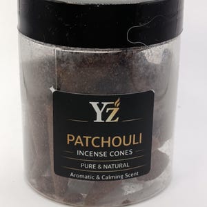 Peut inclure: Un pot en plastique transparent avec un couvercle noir rempli de cônes d'encens bruns. Une étiquette noire affiche le texte "YZ PATCHOULI INCENSE CONES PURE & NATURAL Aromatic & Calming Scent". Le pot est rempli de cônes d'encens brun foncé.