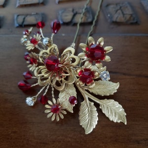 Peut inclure: Une &eacute;pingle &agrave; cheveux dor&eacute;e avec des accents de cristaux rouges. La broche pr&eacute;sente des motifs floraux et de feuilles, avec des grappes de cristaux rouges et de strass transparents. Cet accessoire pour cheveux est con&ccedil;u pour les occasions sp&eacute;ciales.