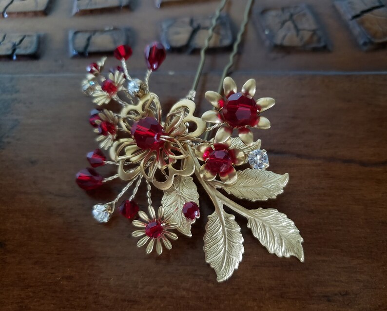 Peut inclure: Une &eacute;pingle &agrave; cheveux dor&eacute;e avec des accents de cristaux rouges. La broche pr&eacute;sente des motifs floraux et de feuilles, avec des grappes de cristaux rouges et de strass transparents. Cet accessoire pour cheveux est con&ccedil;u pour les occasions sp&eacute;ciales.